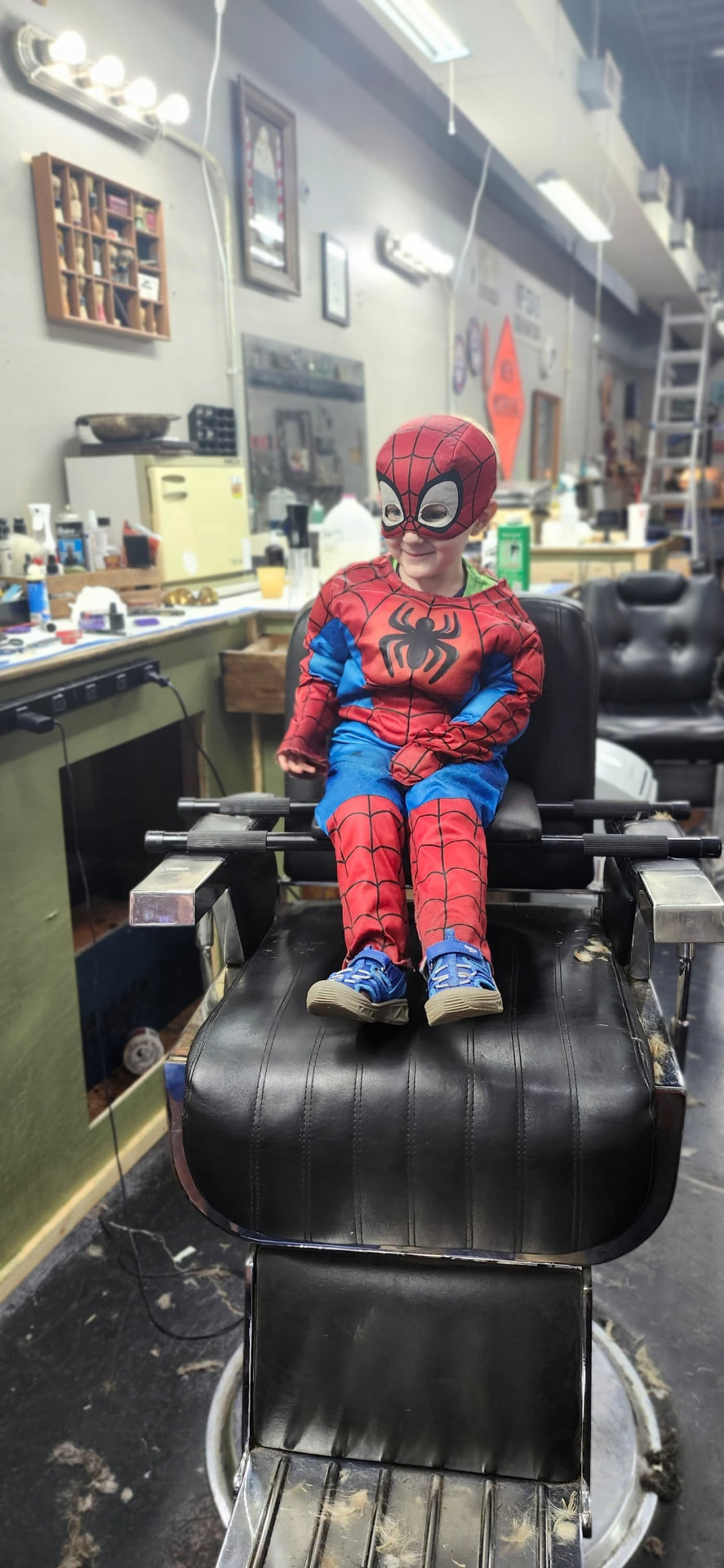 Kid in a Spider-Man costume in the barber chair